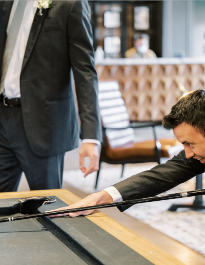 Two men in suits playing pool indoors; one is preparing to hit the cue ball while the other observes.